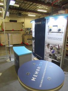 VK-1334 Modular Exhibit with Closet Storage, Reception Counter w/ Storage, MOD-1453 Bistro Table with Wireless Phone Charging, and MOD-1431 Charging Tower with Graphics