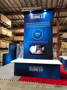 RENTAL: RE-9138 Island Design with 16’ High Gravitee Panel System Tower with Balck Laminated Ceiling Soffit with Recessed Puck Lights, Locking Door, Large Monitor Mount, 55" Monitor, (3) 3' Wide x 15' High Double-Sided Lightboxes, Large Rectangular Coun