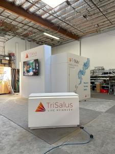 RENTAL: Island Design with Gravitee Conference/Storage Room at 10' High with 12' High Tower, (2) Large Monitor Mounts, 85" Monitor, 55" Monitor, RE-1577 White Laminated Reception Counter, (2) RE-1594 Workstation Counters, Stand-Off Extrusion Frames Inside