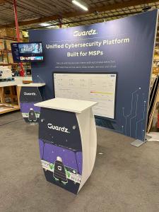 RENTAL: RE-1094 Symphony Inline Design with Concave Curved SEG Extrusion Frame, SYM-401 Workstation Counter with Wireless Charging Ports, Monitor Mount, RE-1255 Reception Counter, (2) LED Arm Lights, 32” Monitor, SEG Fabric Graphic, Direct Print Sintra