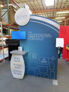 Symphony Portable Traveling Displays with SEG Fabric Graphics, Floating Graphics, Workstation Counter, Monitor Mount, Literature Tray Mount, Wireless Charging Pads, and Rear SEG Graphic