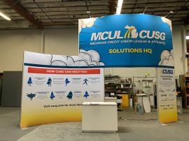 RENTAL: Modified RE-9135 Island Design with 16 ft. High Curved Gravitee Panel System Wall, (8) LED Arm Lights, RE-1576 Reception Counter with Recessed RGB Accent Lighting, and SEG Fabric Graphics