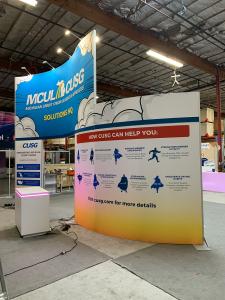 RENTAL: Modified RE-9135 Island Design with 16 ft. High Curved Gravitee Panel System Wall, (8) LED Arm Lights, RE-1576 Reception Counter with Recessed RGB Accent Lighting, and SEG Fabric Graphics -- View 2