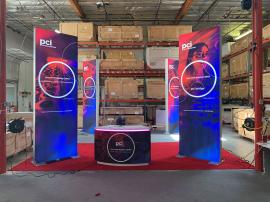 RENTAL: Island Design with (4) 4' Wide x 12' High Double-Sided Lightboxes, RE-1597 Curved White Laminated Reception Counter, Large Monitor Mount, SEG Backlit Fabric Graphics, and Vinyl Applied Graphic