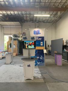 RENTAL: RE-9068 Island Design with 10 ft. High Storage Tower with Locking Door, Bridged Extrusion Beams From Storage Tower to (3) Kiosks, (3) RE-1201 Tapered Counter Workstations, (1) RE-1228 Small Curved Reception Counter, (4) Monitor Mount, (4) RE-170 L