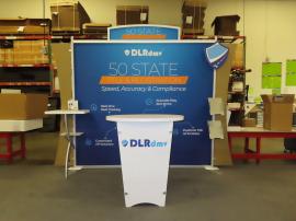 VK-1227 Portable Display with Fabric Graphic, Arch Header, Circle Graphic with Standoffs, Backwall Counter with Wireless Charging Pads, Brochure Holders, Monitor Mount, LED Stem Lights, and LTK-1001 Counter with Locking Storage