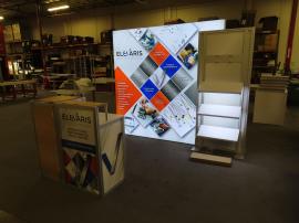 Modified ECO-1070 Sustainable Exhibit with Aluminum Extrusion Frame, Backlit Tension Fabric Graphic, Modifed ECO-35C Counter with Locking Storage, (3) Angled Product Shelves, and Monitor Mount