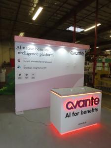 Custom Inline Exhibit with SEG Fabric Backwall, Laminated Header, Puck Lights, Monitor Mount, and Modifited MOD-1596 Counter with RGB Halo Light Logo and Locking Storage